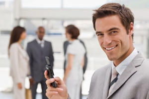 Closeup of happy young businessman text messaging on cellphone with colleagues in the background